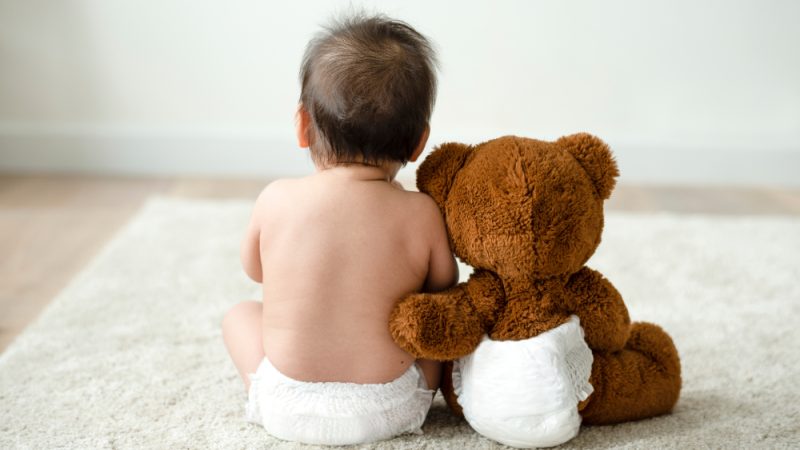 Back of a baby and a stuffed teddy bear in nappies